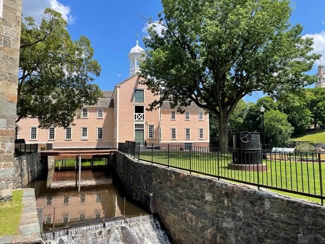 Slater summer Waterway with waterfall in foreground and 2 1/2 story peach-colored wooden building in background