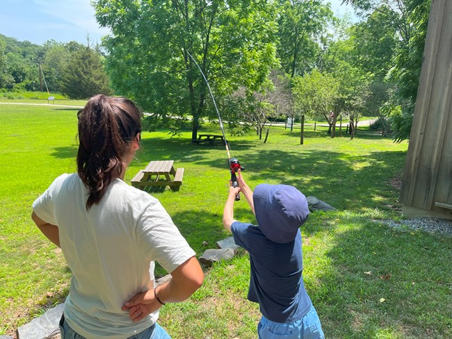 Sofia and angler practicing Intern standing next to young boy holding a fishing pole