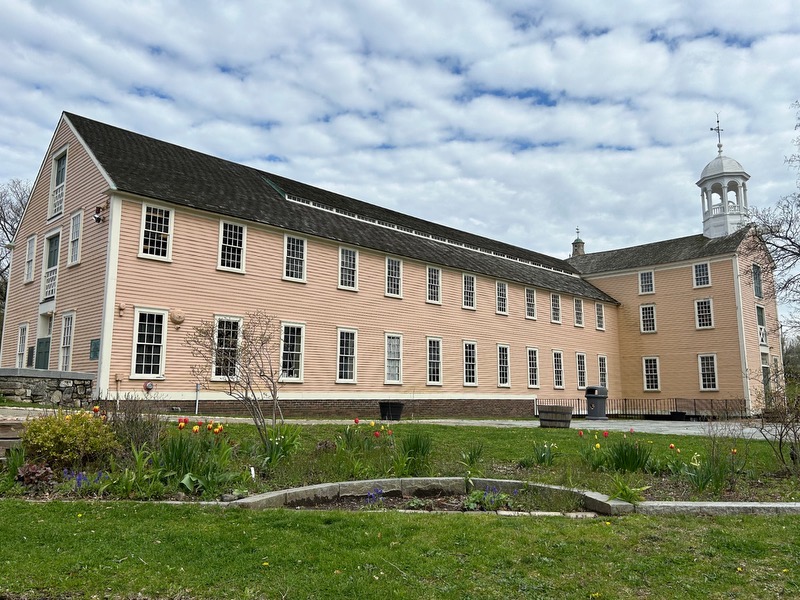 Spring newsletter Two story yellow mill building with flowers in the foreground
