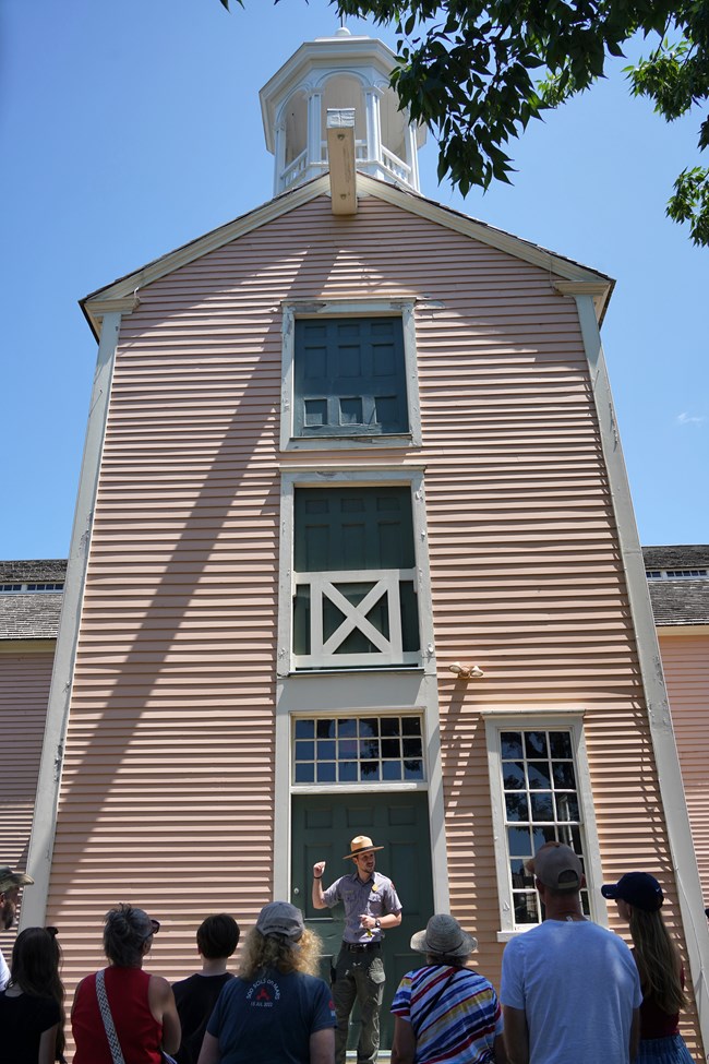 Tyler Tour Park Ranger stands in front of Old Slater Mill belltower in front of group of visitors