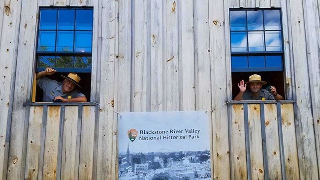 Two Park Rangers wave from the windows of the Kelly House Barn