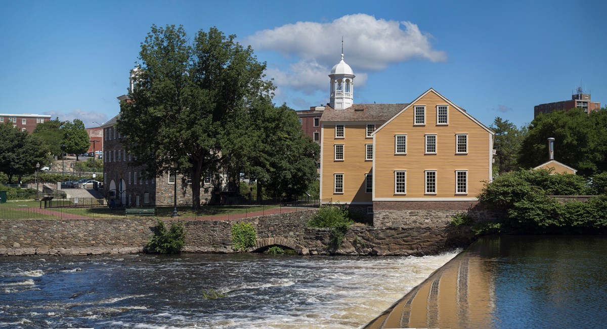 Yellow wooden mill structure on the banks of the Blackstone River