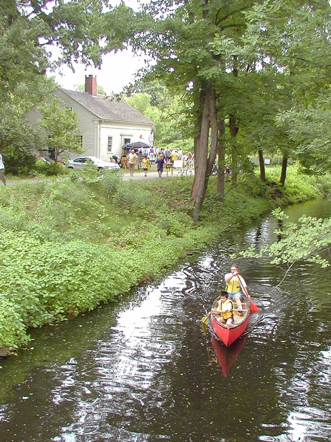 Two people paddle down Blackstone Canal adjacent to Kelly House