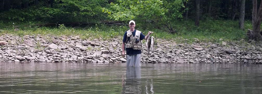 fisherman standing in river holding fish