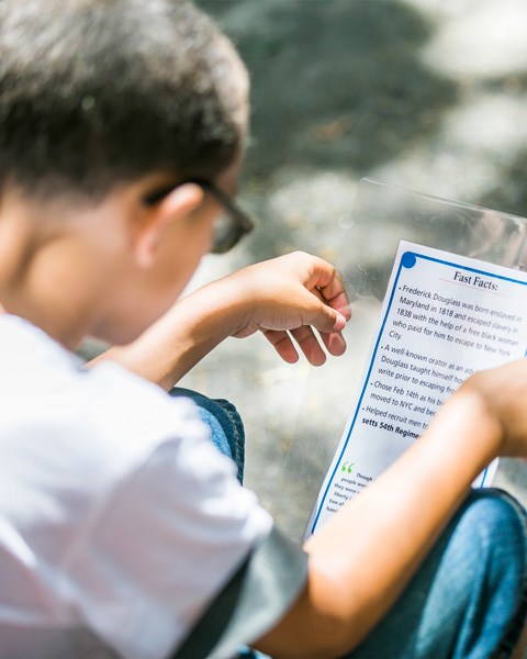 Looking over the shoulder of a young student. Student is holding and studying a card with the title "Fun Facts"