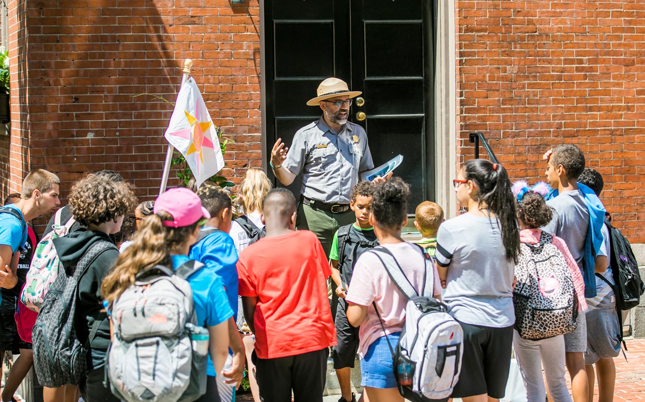 Ranger standing in front of a building speaking to a group of youth.