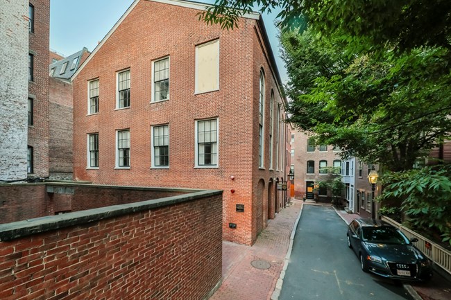 A-frame, 3 stories, rectangular red brick building with grid-paned windows on short end and tall arched windows on long end.