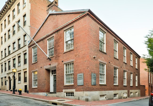 3 floor red brick rectangular building with grid paned windows across floors.