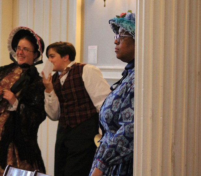 Park Rangers dressed in 19th century clothing listening to visitors participating in a recreated town meeting.
