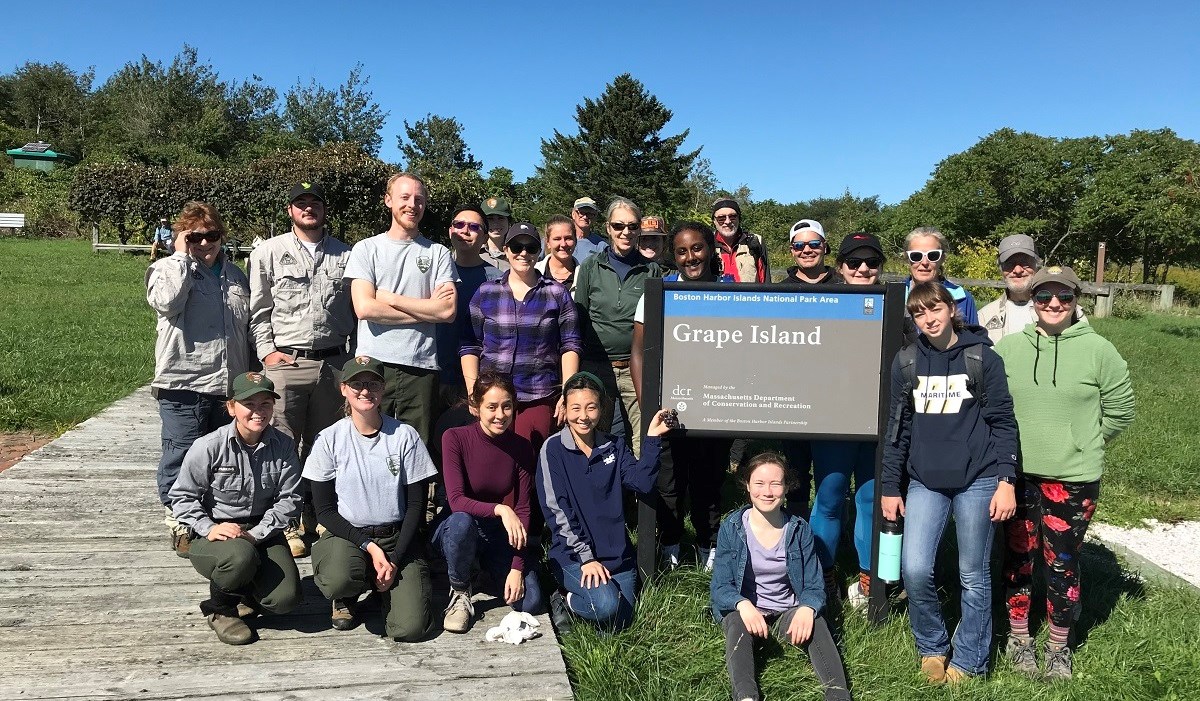 group of people in uniform or casual clothes standing around a Grape Island sign.