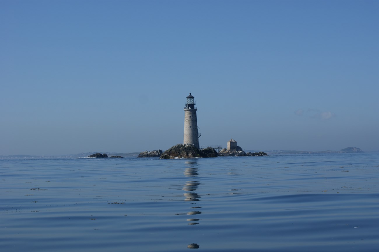 a white lighthouse sits on a small rocky island surrounded by calm water.