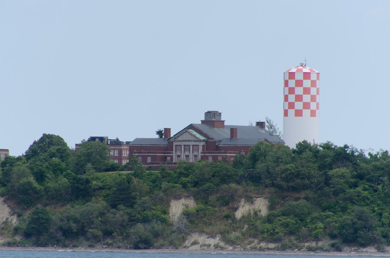 On the top of an island hill, a red checkered water tower stands next to a large brick structure.