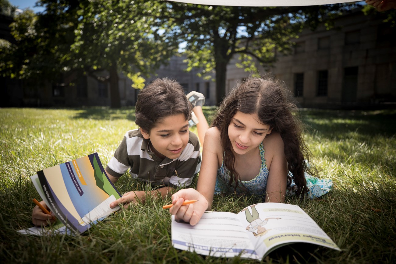 boy and girl lying on grass looking at jr. ranger book