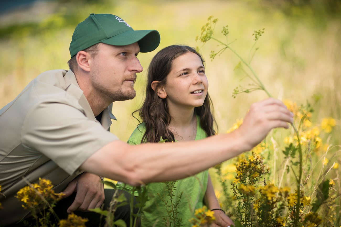 DCR ranger kneeling next to girl, both looking at flowers