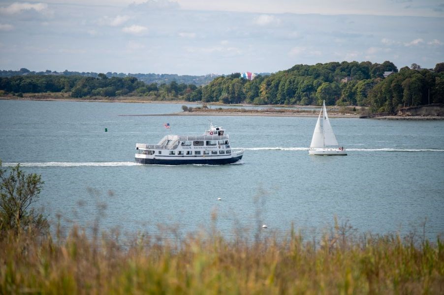 a ferry and a sail boat glide on the water between two islands in Boston Harbor