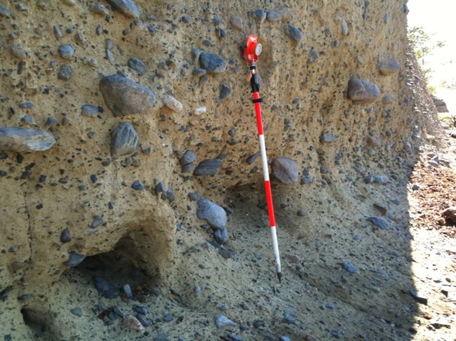 exposed bluff of cemented rocky sediments with a orange and white pole leaning against it