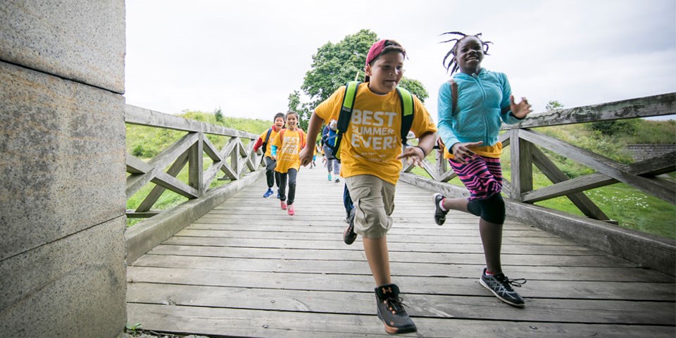 Young visitors run toward camera over a wooden footbridge.