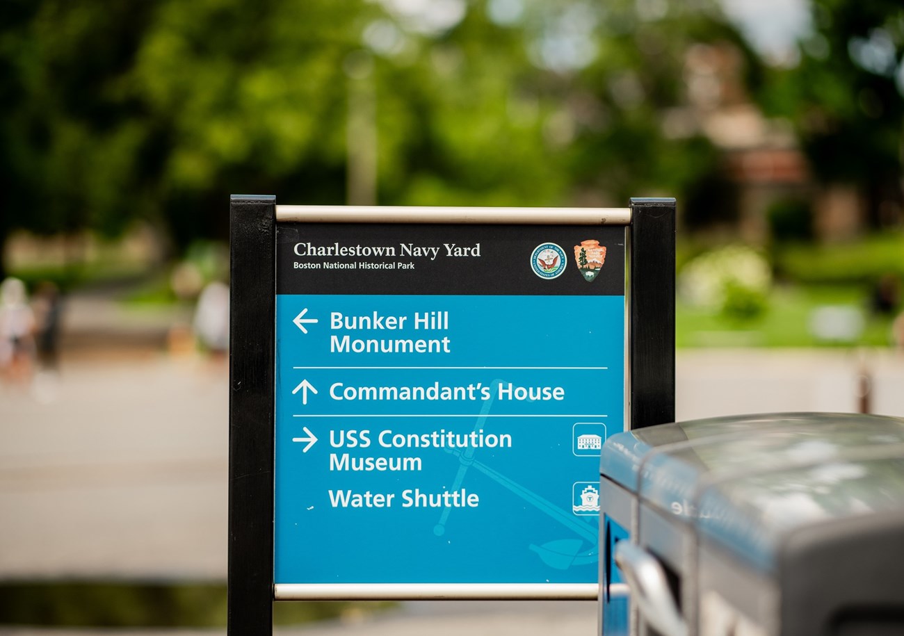 National Park Service Sign with blue background and white text and arrows directing people to locations at the park.