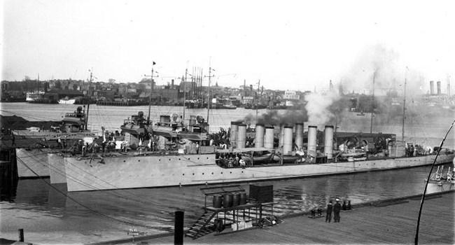Three steel destroyers with four smokestacks are moored along a pier in the Navy Yard.