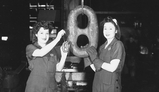 Two women shipyard workers standing next to a die-lock chain.