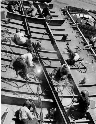 Black and white photograph of many women spread out and welding plates together to form a hull.