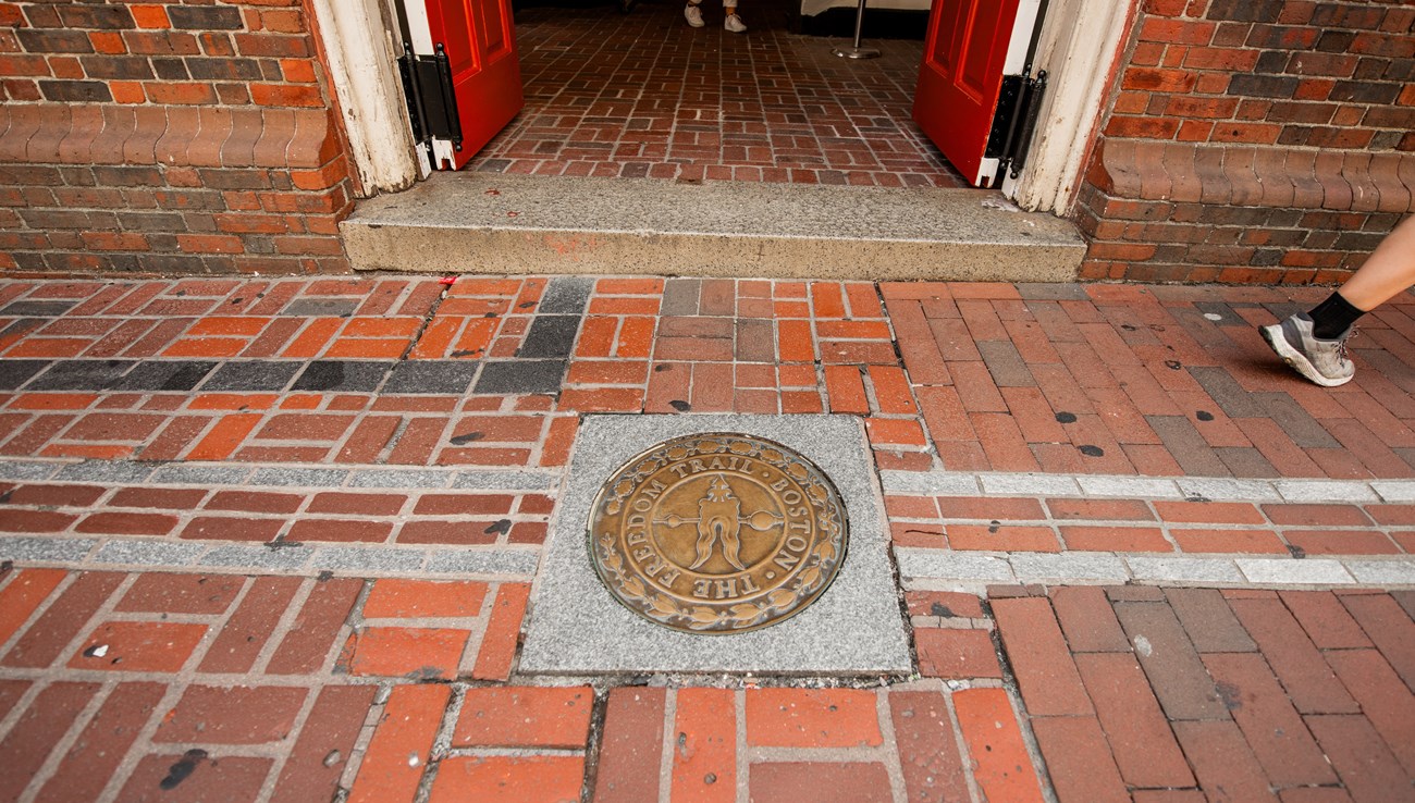 Brick path with the Freedom Trail marker pointing into a historic site.