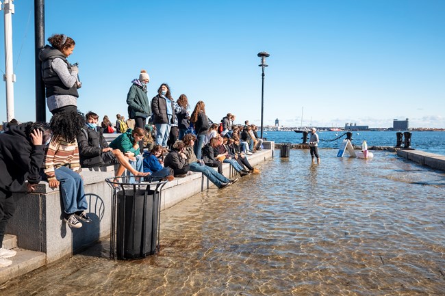 people sitting on a series of steps at the end of a wharf that is flooded.