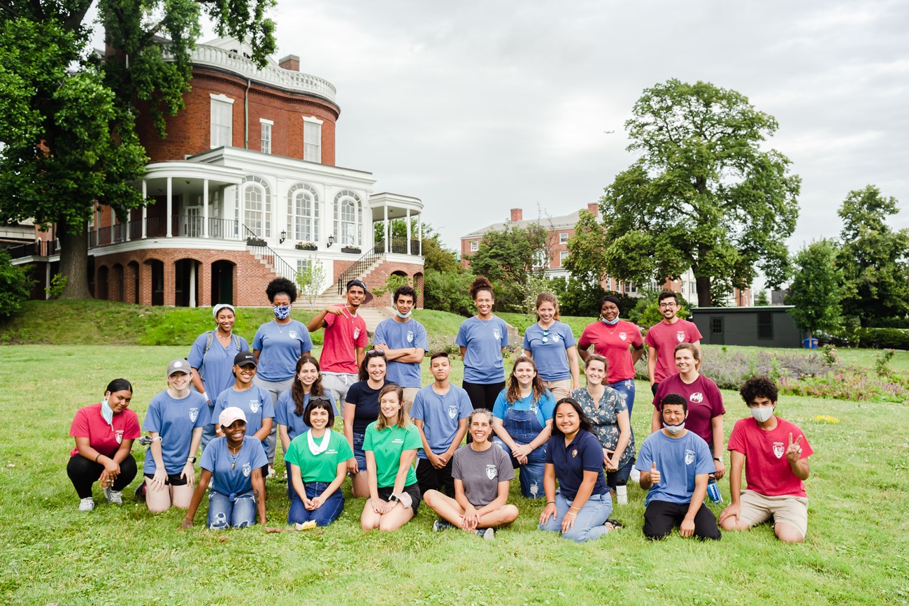 Group photo of youth employees and Rangers standing outside in front of a house.