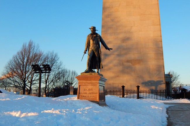 The Prescott Statue in front of the Bunker Hill Monument surrounded by snow.