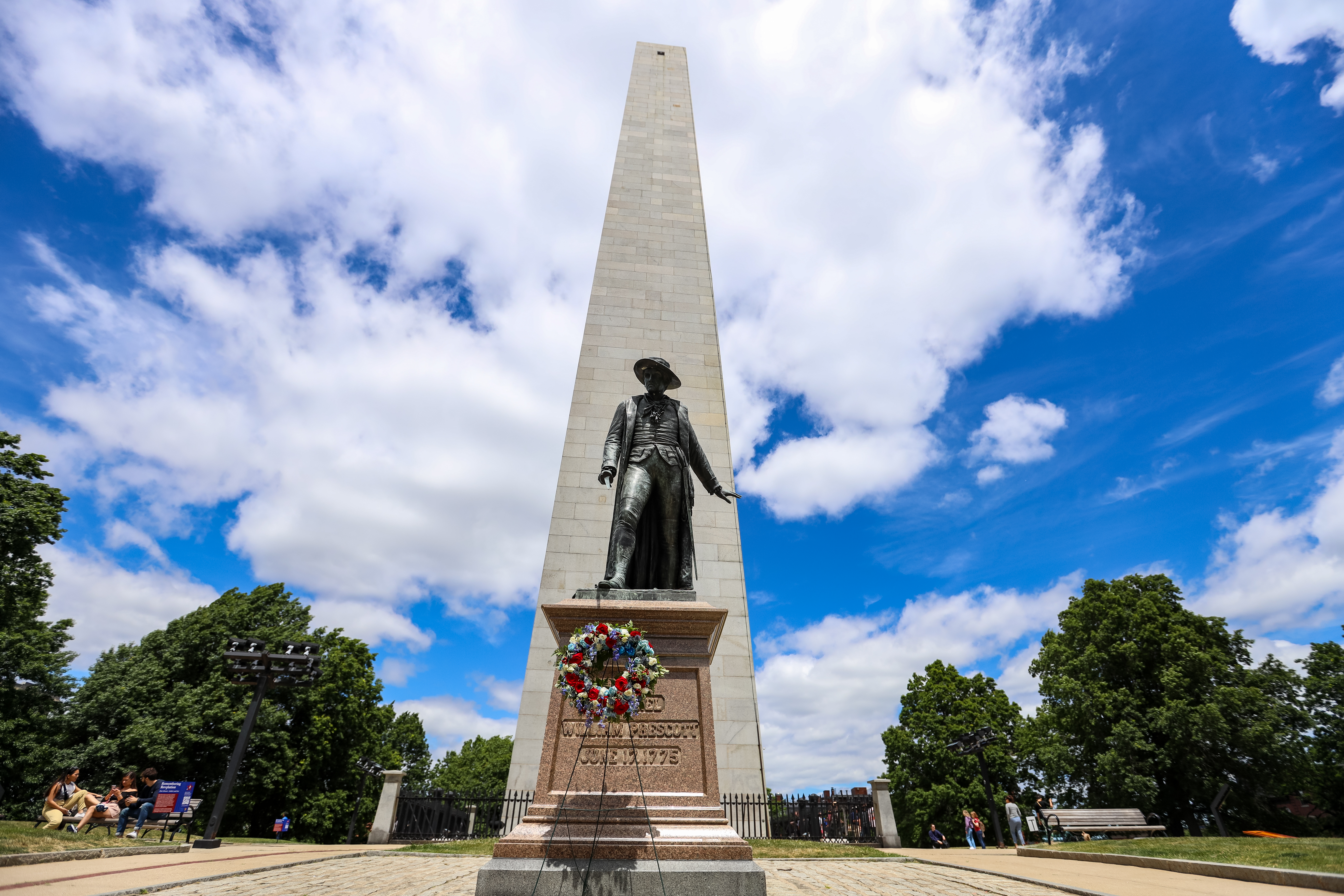 Bunker Hill Monument-Wreath Bunker Hill Monument with the Prescott Statue before it. On a stand in front of the statue is a red, white and blue decorated wreath. A blue sky is filled with white clouds.
