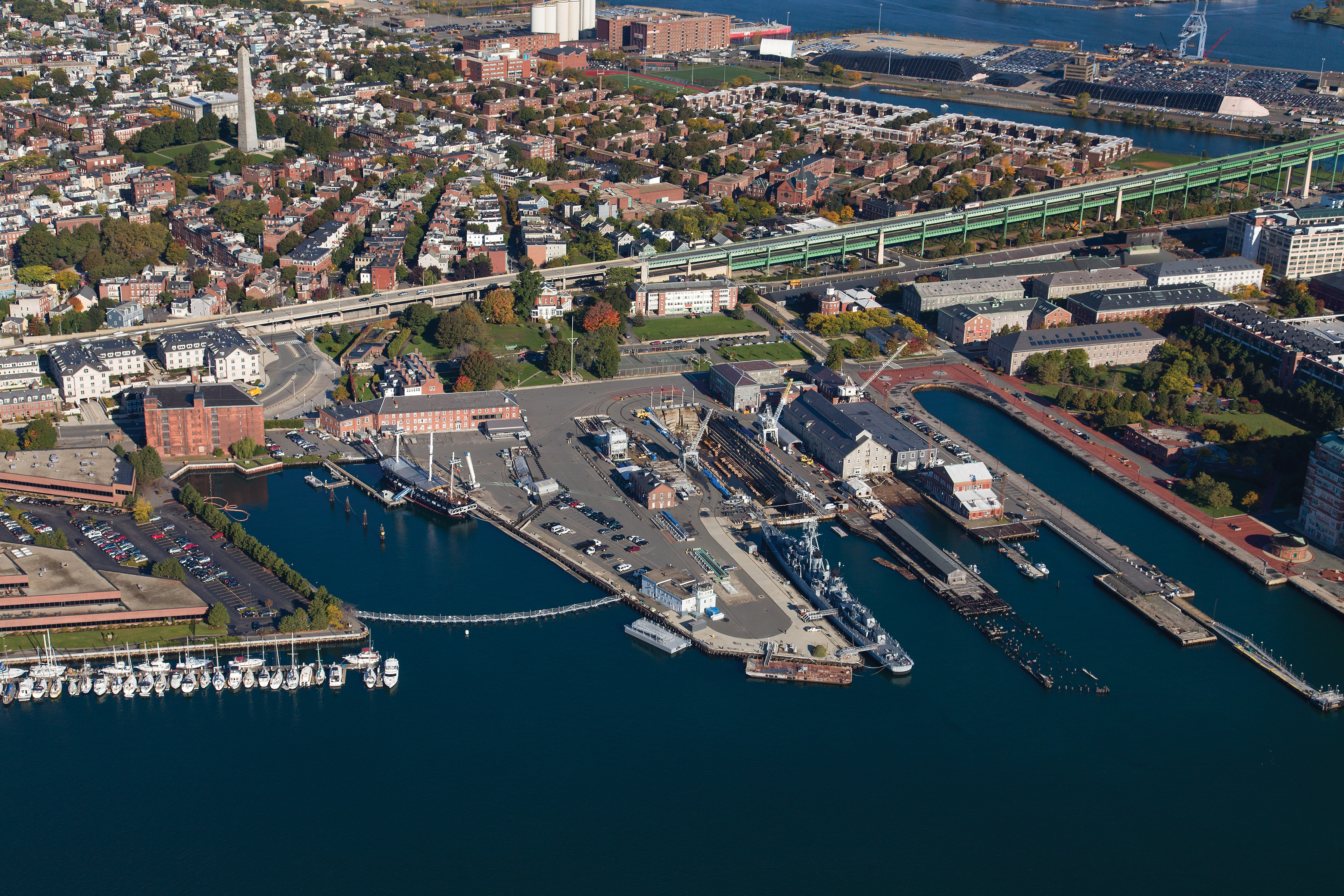Aerial photograph captures the land, water, ships, and structures present in Charlestown Navy Yard of Charlestown, Massachusetts.