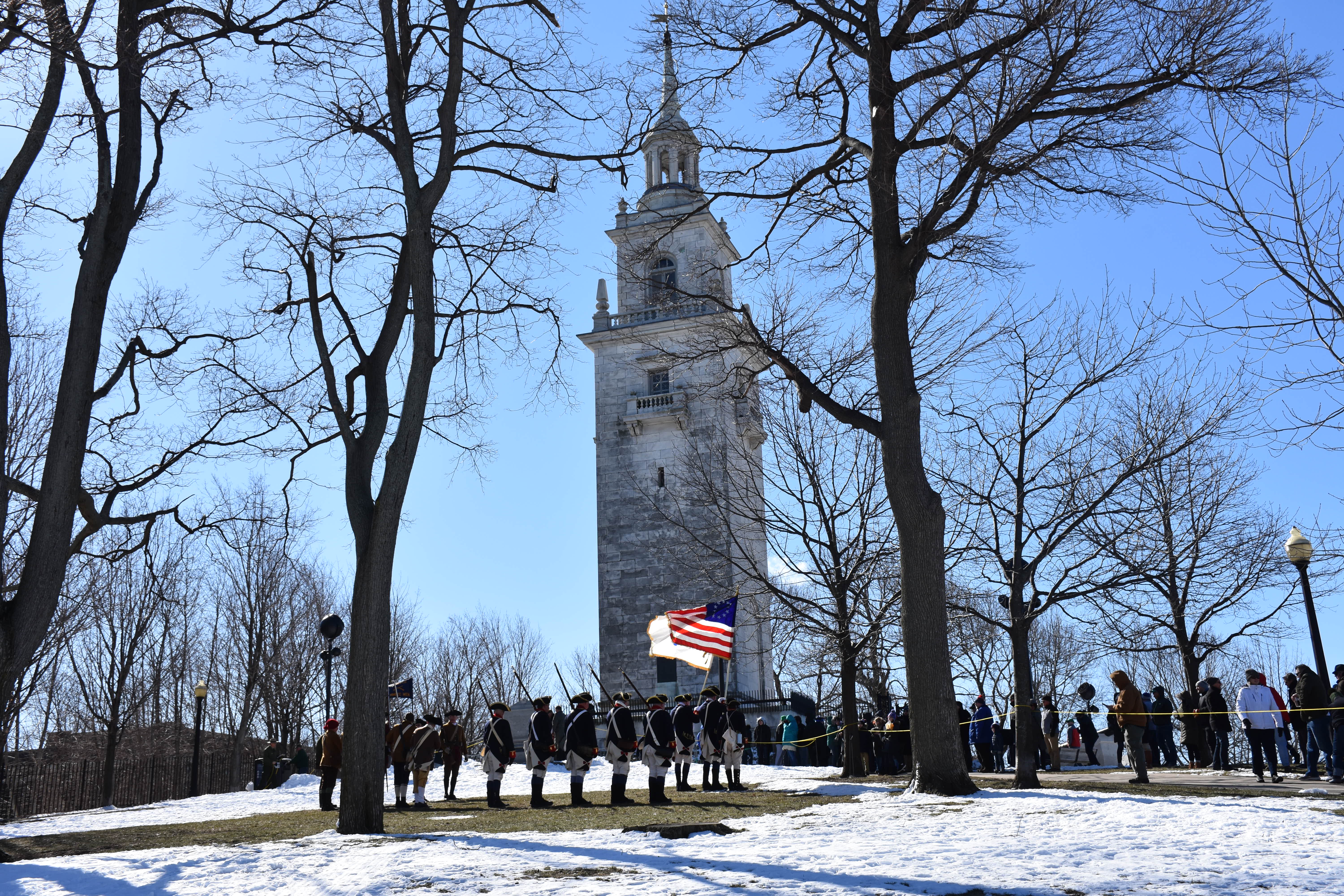 wintry view of Dorchester Heights monument through the bare tress. ROTC members posting flags in the foreground
