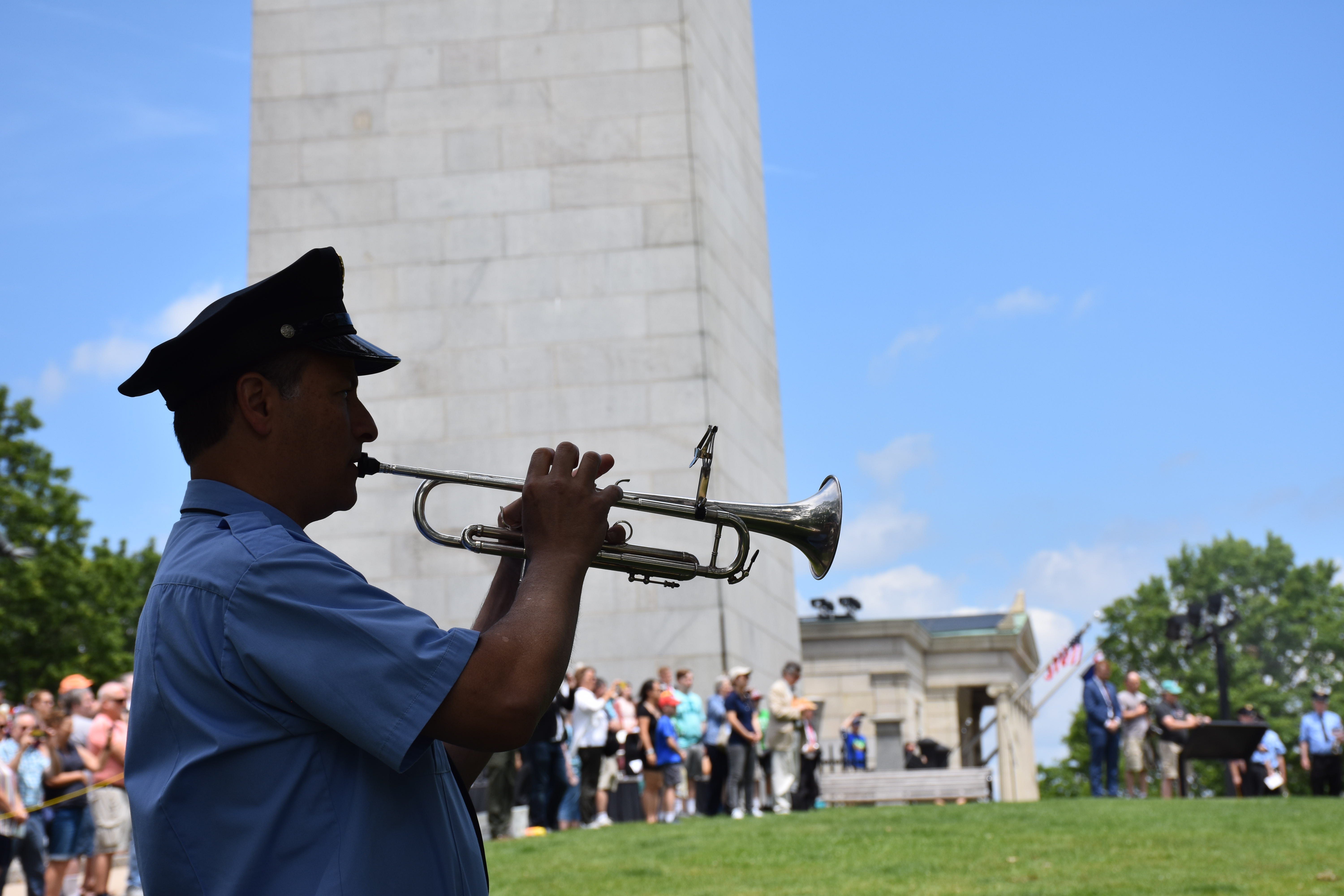 Bugler playing in front of the Bunker Hill Monument. He is in the shade with the Monument in the sun.