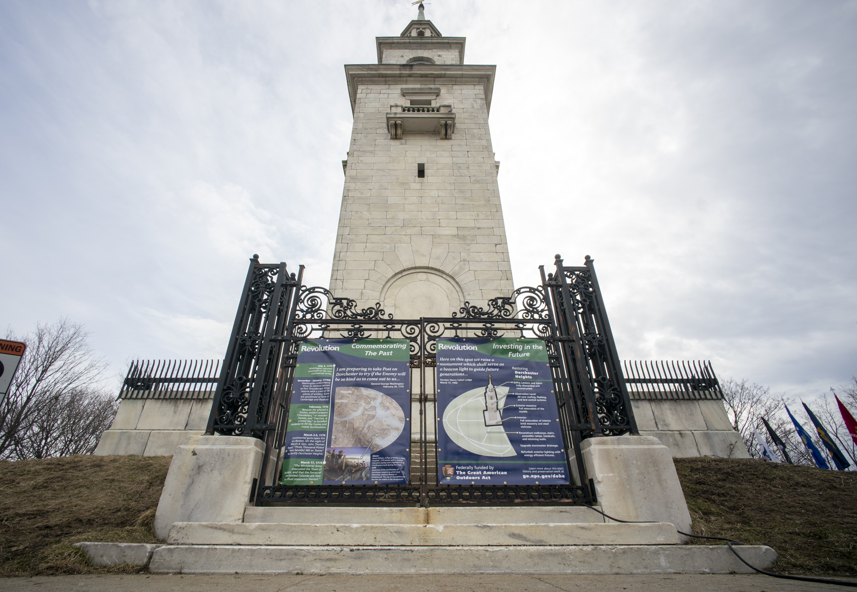 Teuten-PressRelease Dorchester Heights Monument with gates closed and vinyl exhibit on the history and restoration project on doors.