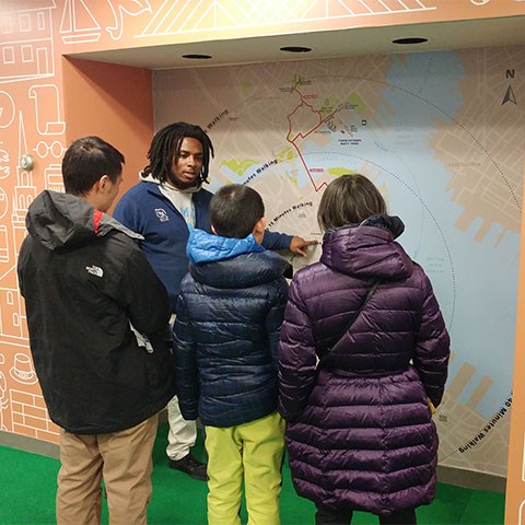 Park staff member stands in front of large map while showing three visitors the distance between sites.