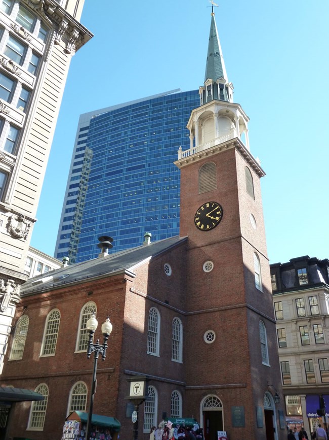 A two story brick church building with arched windows. At the front of the Meeting House is an attached brick belltower with a wood and weathered copper steeple. The tower has a clock face.