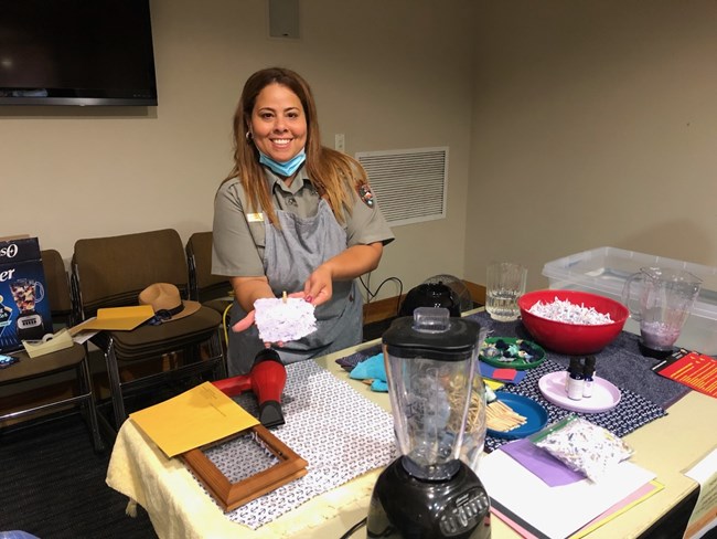 Ranger at a table set up with crafts and holding a piece of home-made paper