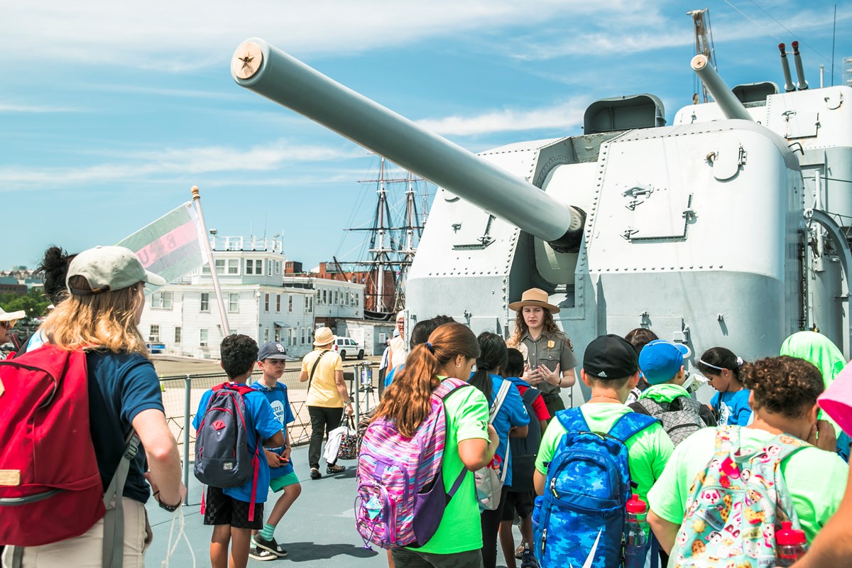 Ranger in front of a gun on the USS Cassin Young speaking with a group of students.