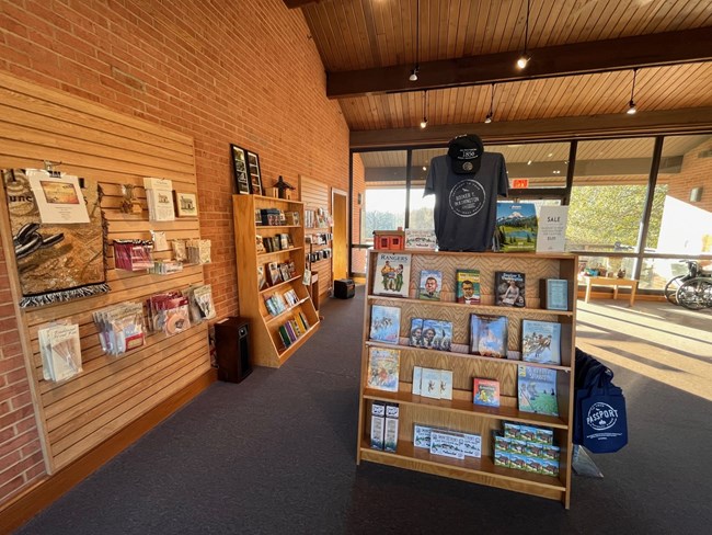An interior view of the Eastern National Bookstore at Booker T. Washington National Monument showing a series of bookcases featuring books, tee-shirts and tote bags.
