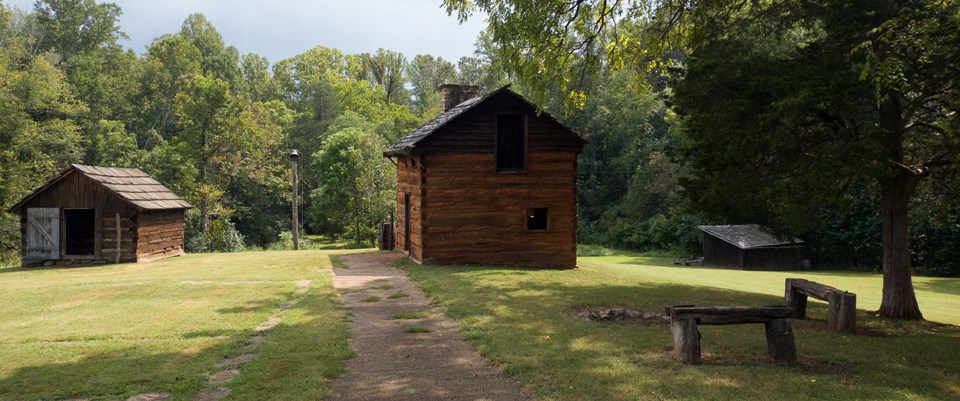 A paved path with a view of a group of rustic cabins.