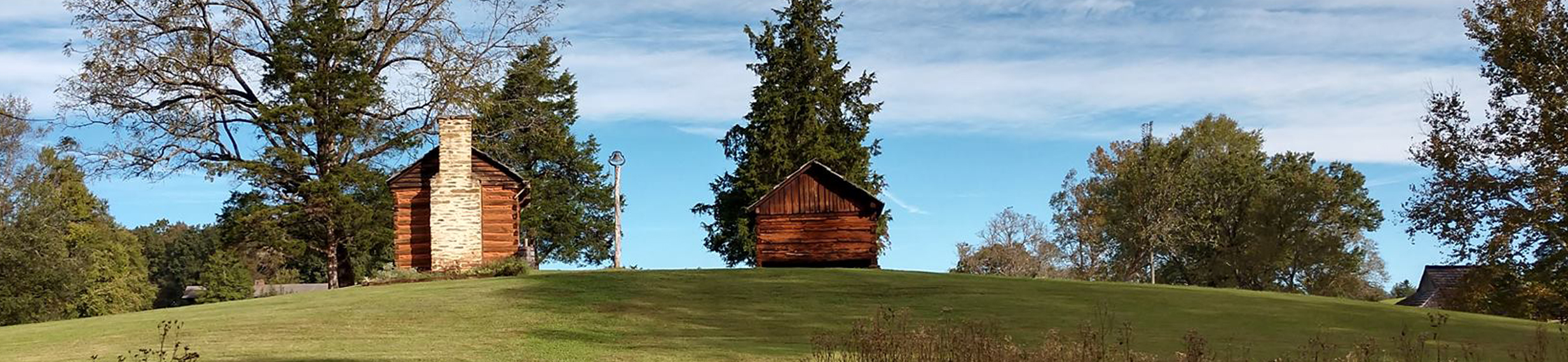 A rolling green hillside with two rustic cabins appearing in the background.