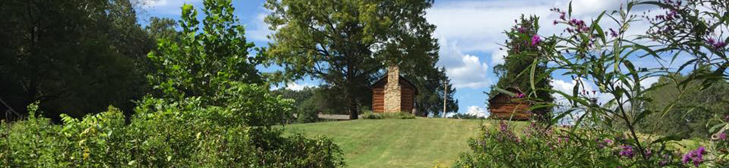 A lush green foreground with an inclined hill and two rustic cabins in the background.