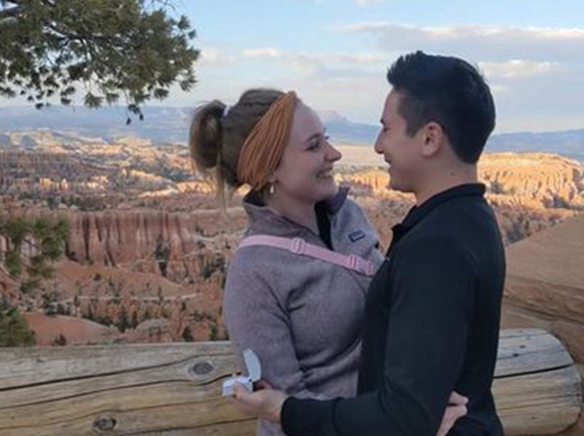 A man and a woman gaze at one another lovingly at a paved viewpoint.