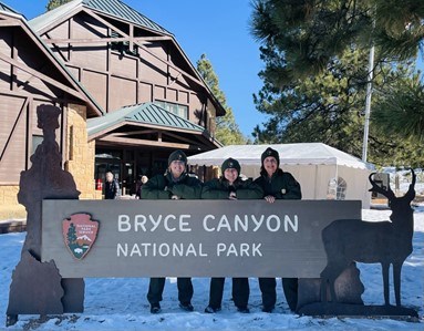 Three rangers stand behind a sign reading Bryce Canyon National Park