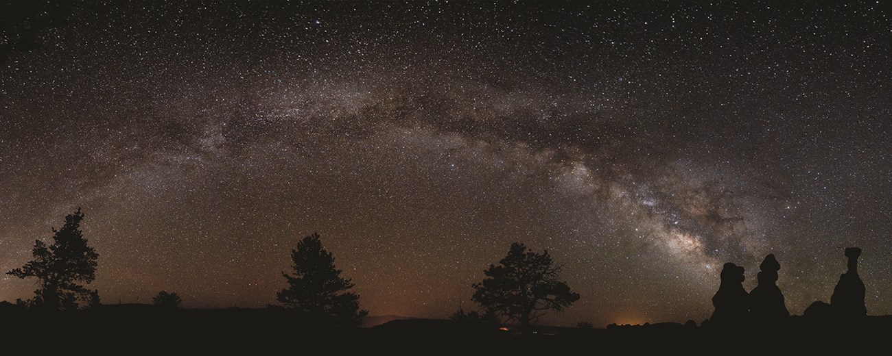 A starry milky way sky above silhouettes of rock spire formations