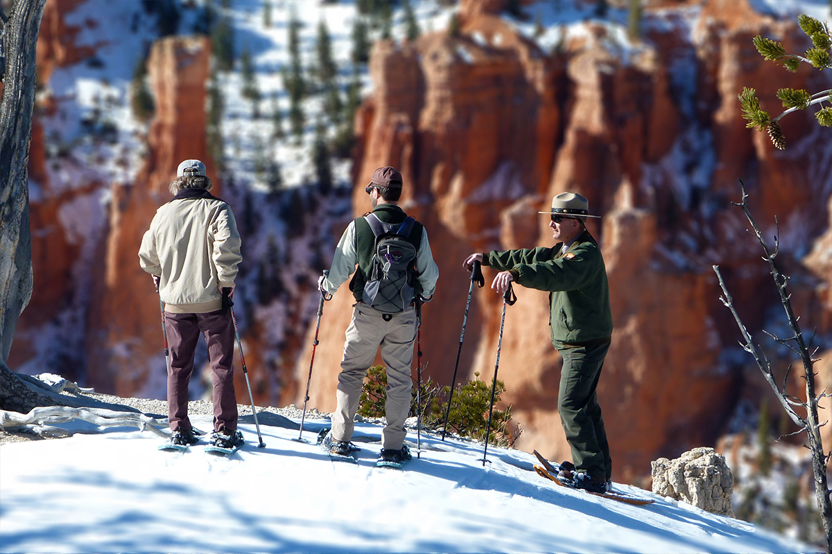 Ranger Stands beside two visitors during a winter snowshoe hike