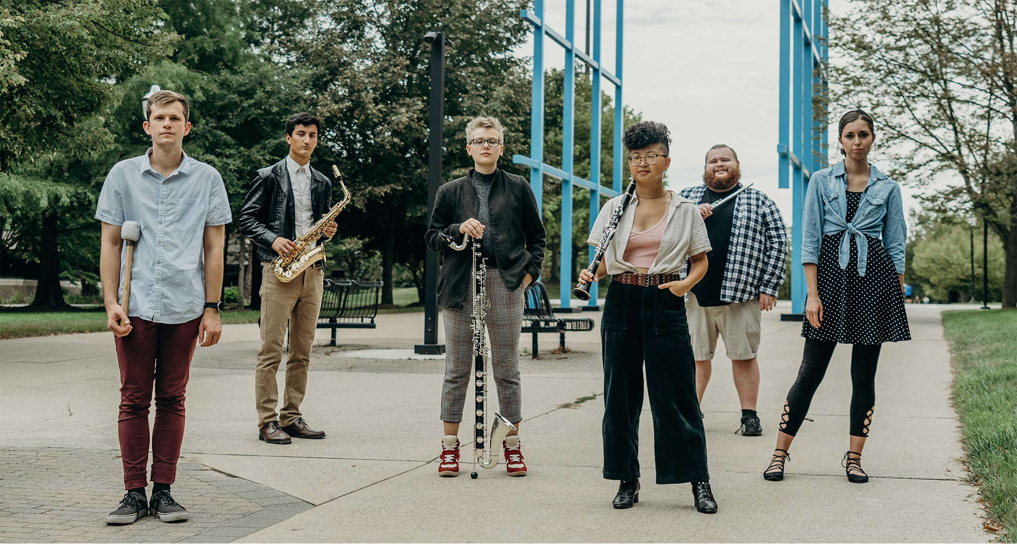 Photo of the Grand Valley State University New Music Ensemble A group of musicians stand holding various woodwind instruments in a paved plazxa.