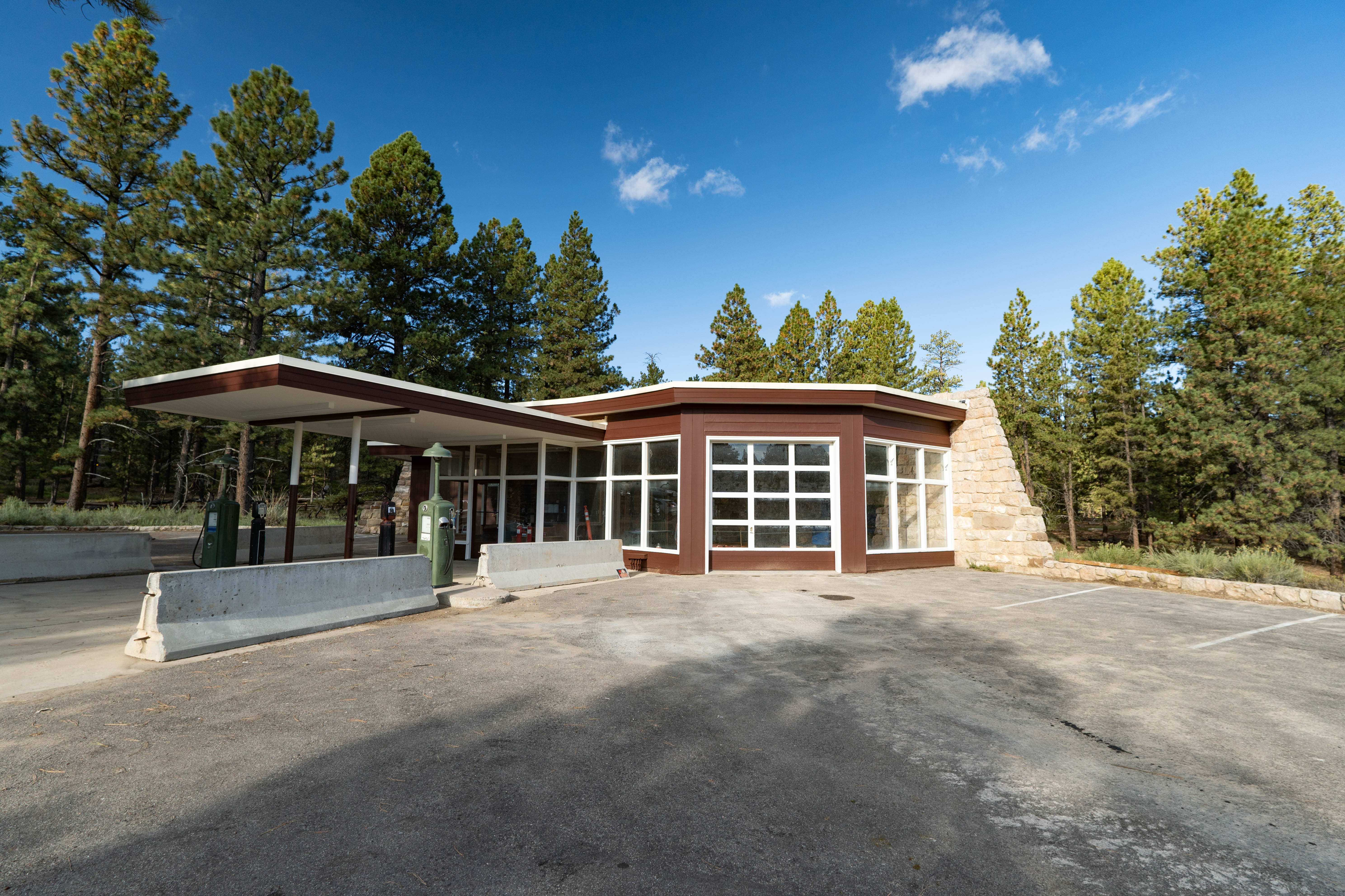 A modernist building painted brown and white with large glass windows and flat roof lines. This is a gas station built in the late 1940s, situated within a pine forest in a small parking lot.