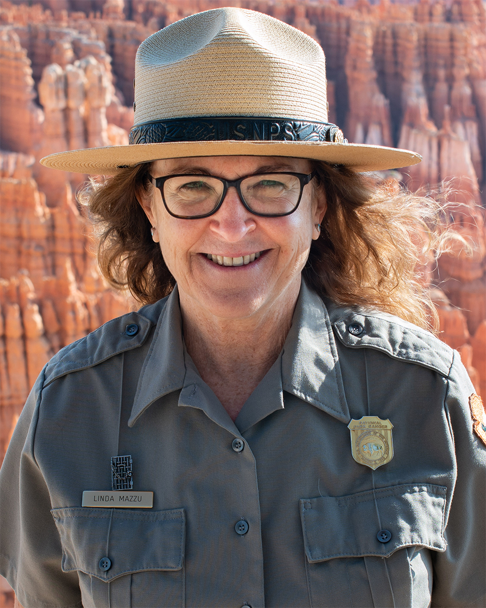 Woman wearing glasses and ranger uniform smiles with background of red and white limestone spires