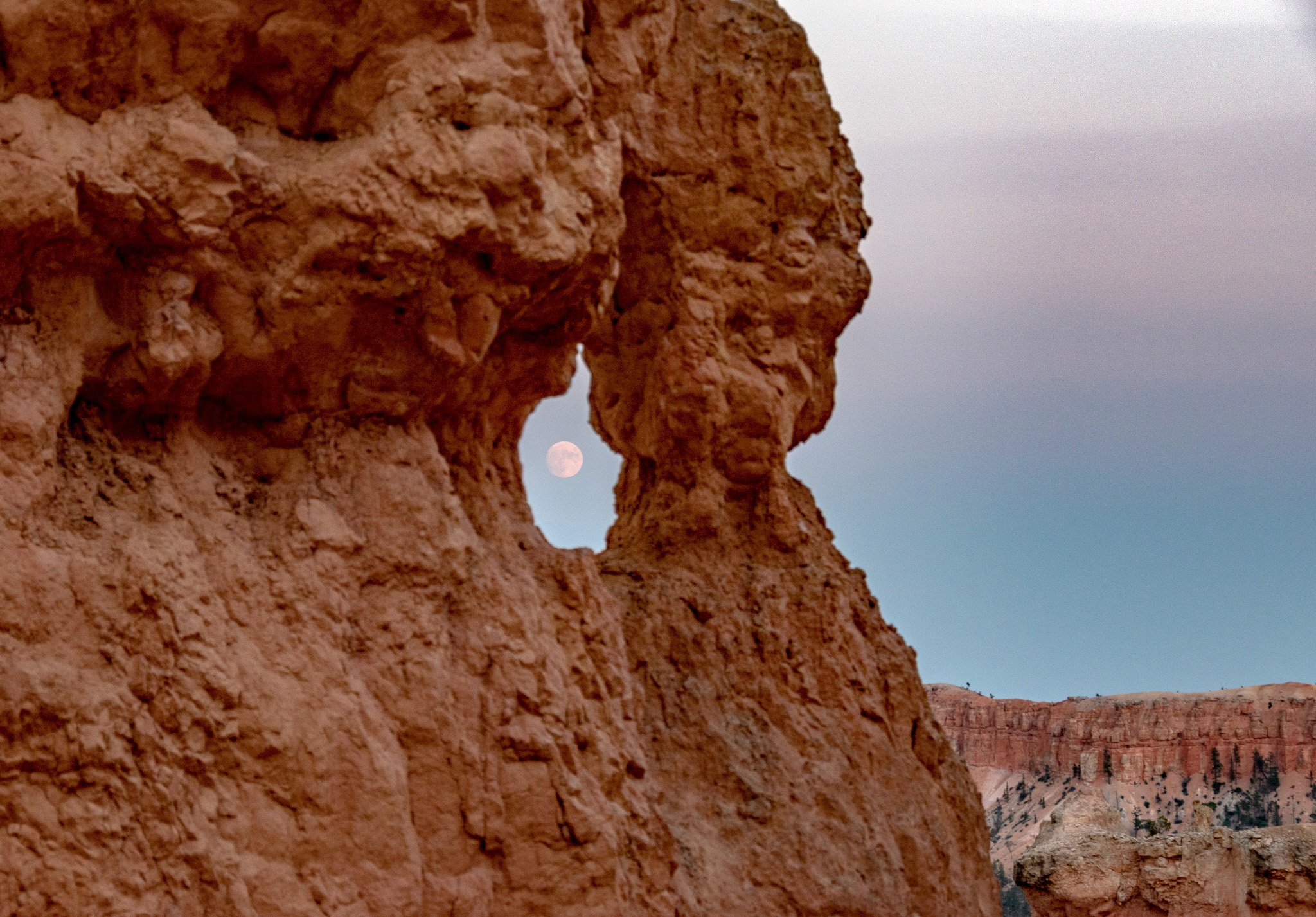 A full moon rising is visible through a hole in a rock wall
